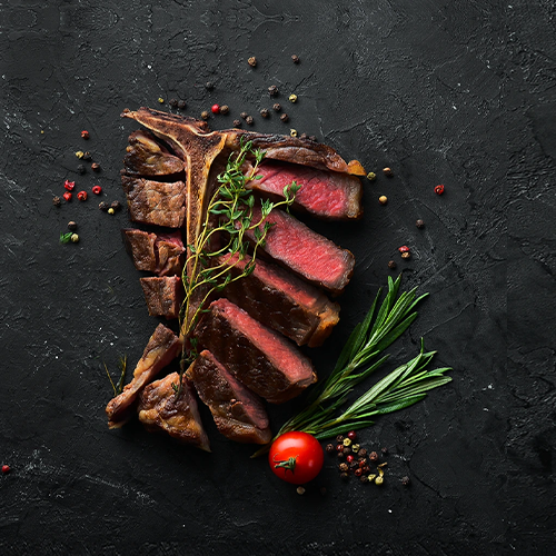Sliced steak with herbs and a tomato on a dark surface
